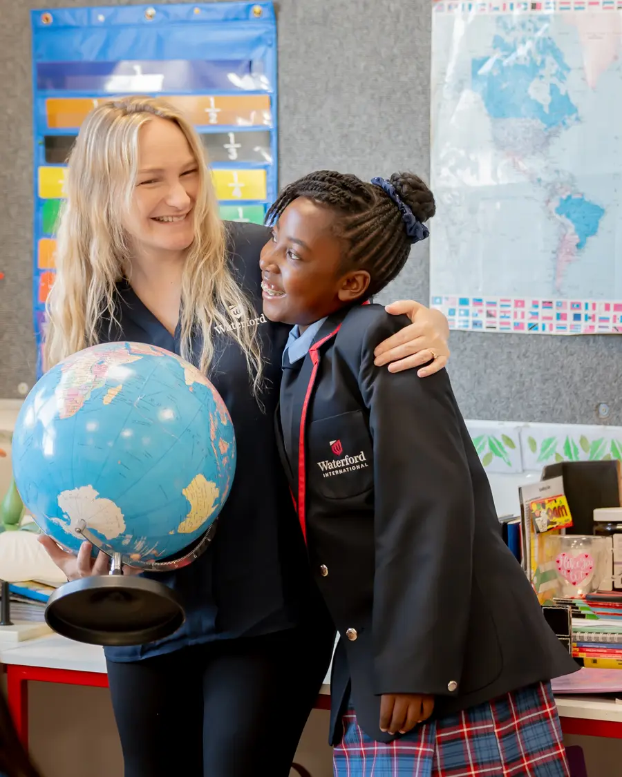 A teacher holding a globe, sharing a laugh with a girl in a blazer