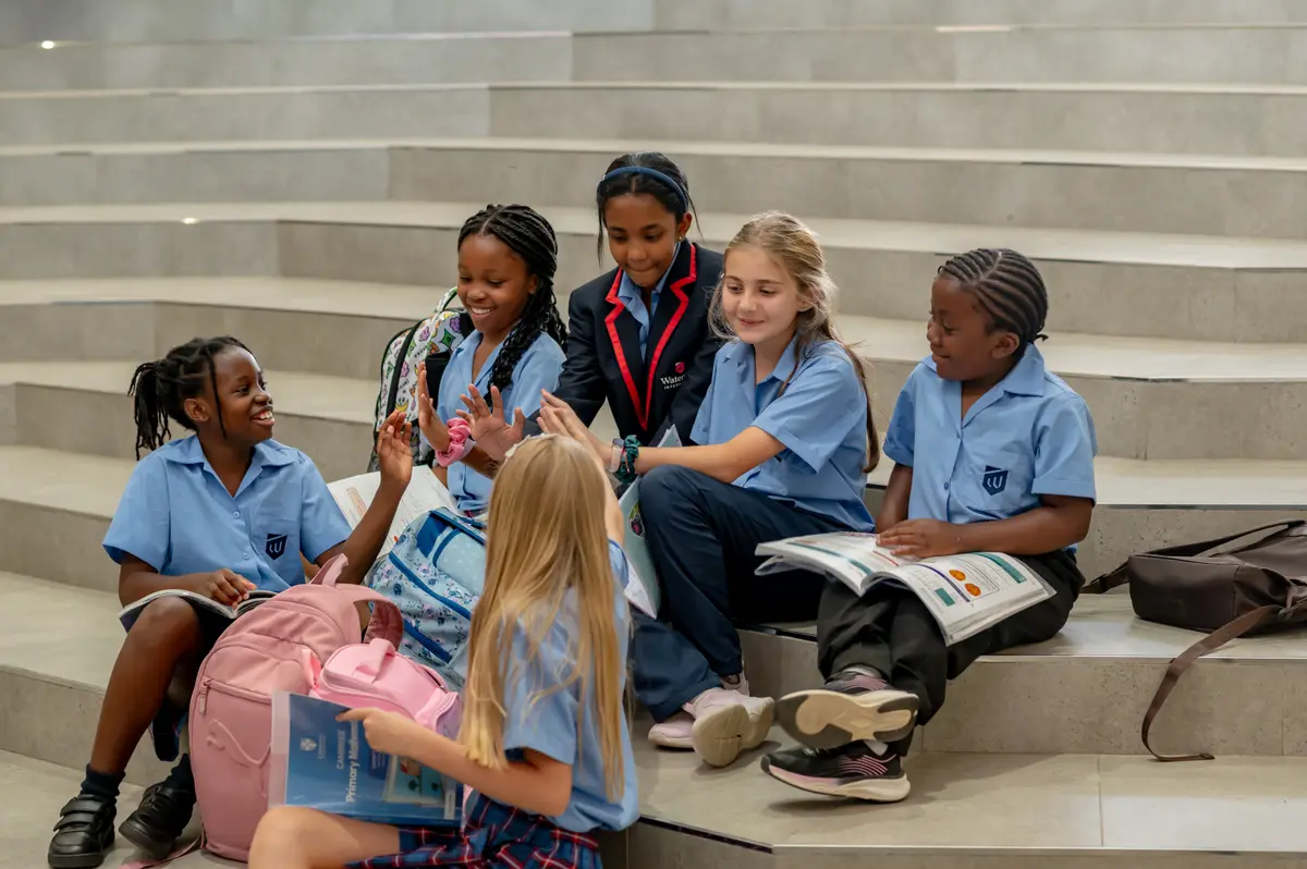 A group of children sitting together on wide steps, chatting with their books