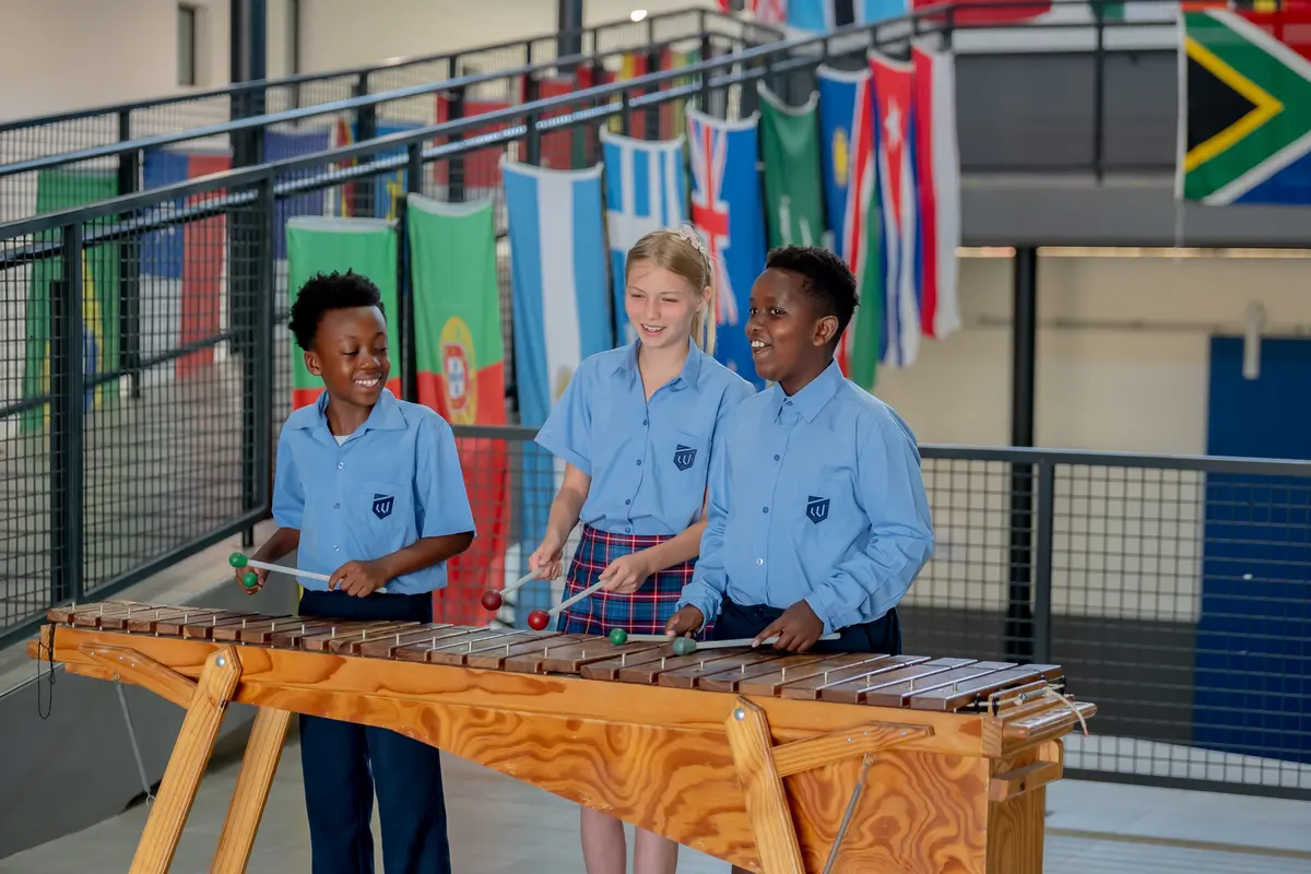 Three children playing the marimba in front of a wall of flags