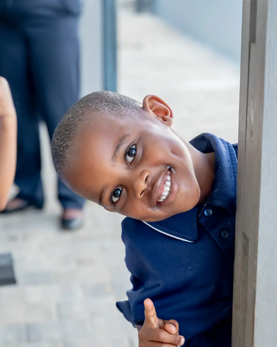 A boy peeking around a doorway with a big smile and a thumbs up