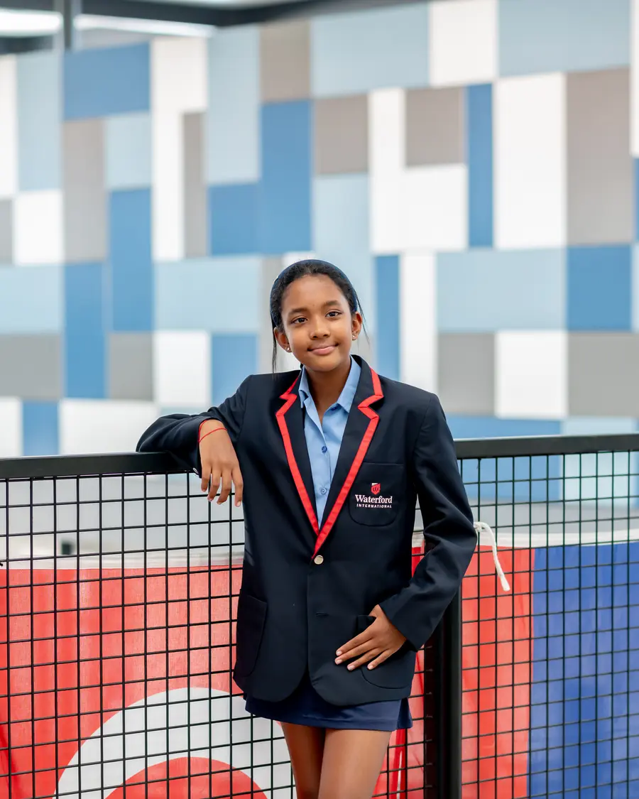 A High School student in a blazer leaning on a railing, smiling