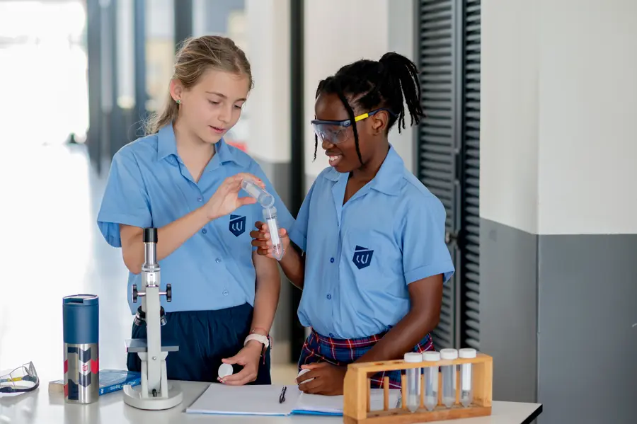 Two girls in safety glasses preparing a slide beside a microscope