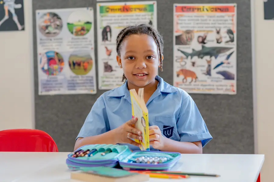 A girl smiling at her desk with a book and a pencil case, in front of a science display