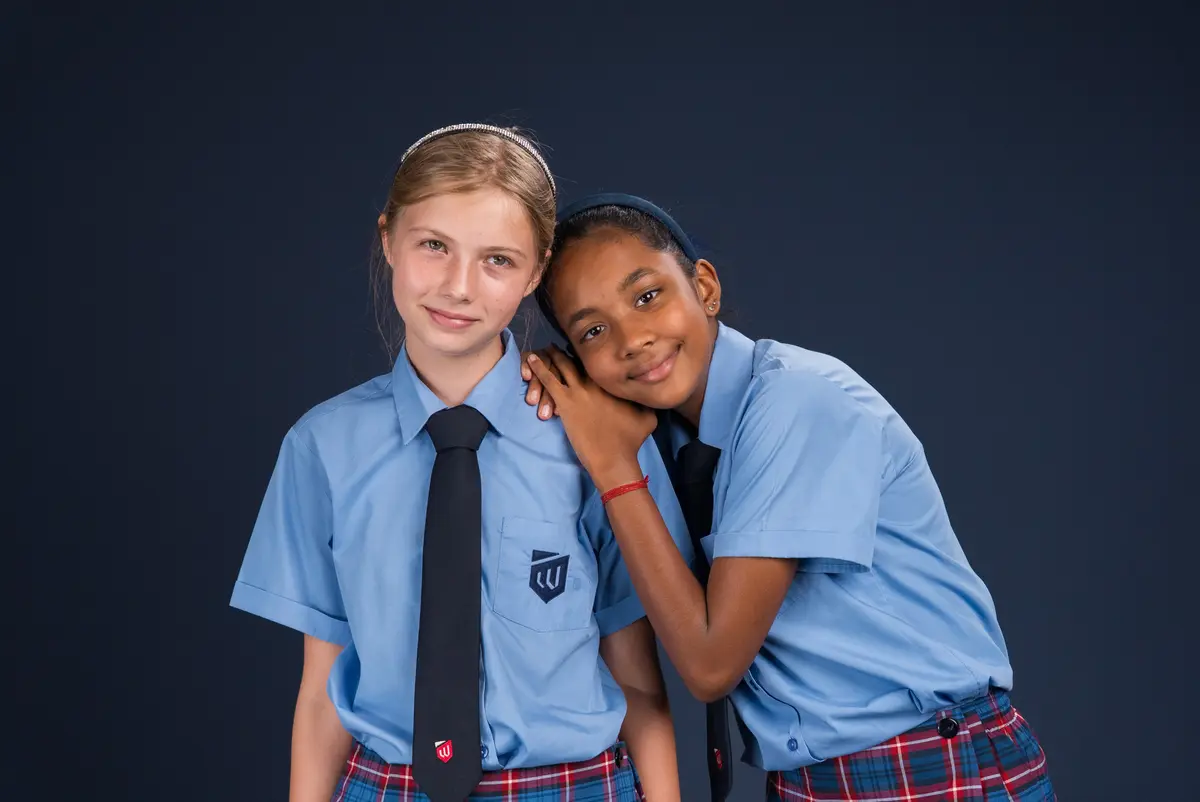 Two girls in school uniform leaning their heads together and smiling