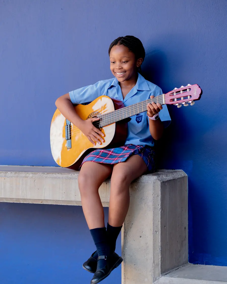 A girl playing guitar against a bright blue wall