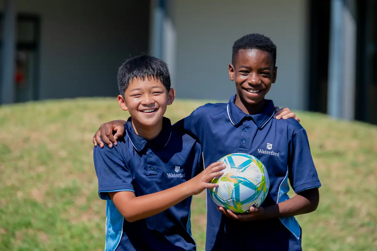 Two boys in sports kit with their arms around each other, holding a soccer ball