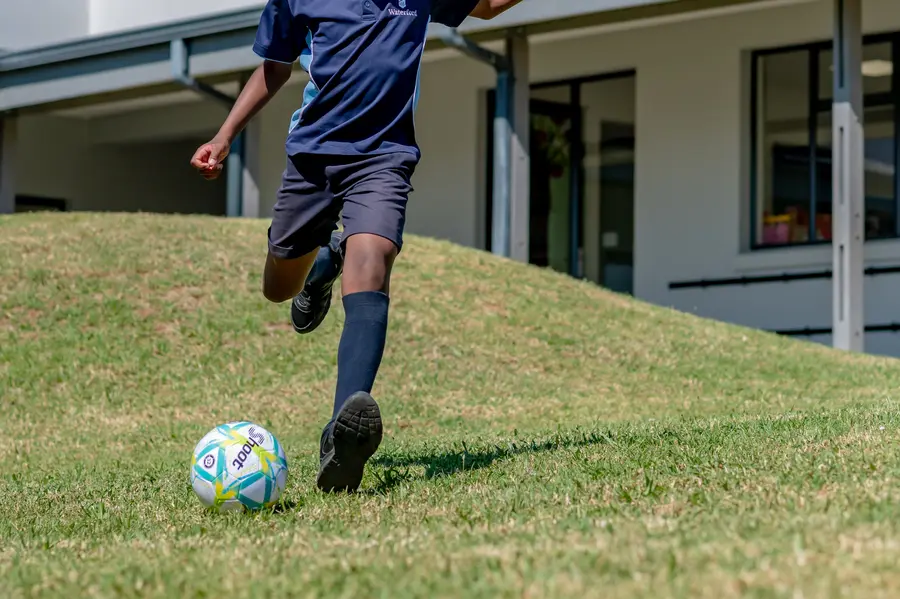 A boy in sports kit about to kick a soccer ball on the grass